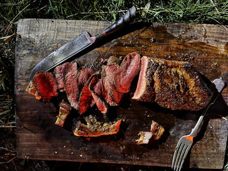Sliced cooked steak on a rustic wooden cutting board with a knife and fork