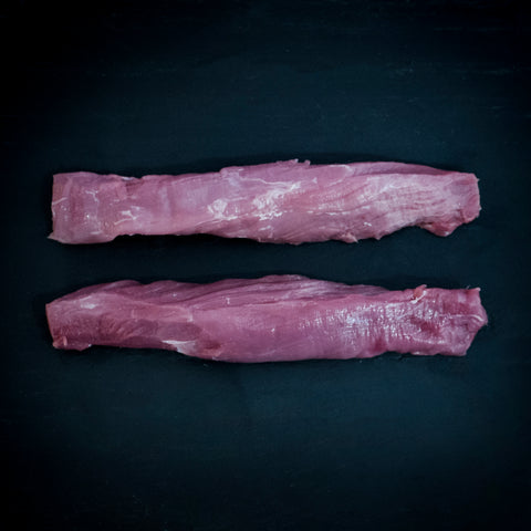 2 pork tenderloins lying parallel on a black background