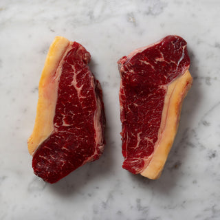 Two raw sirloin steaks on a marble surface