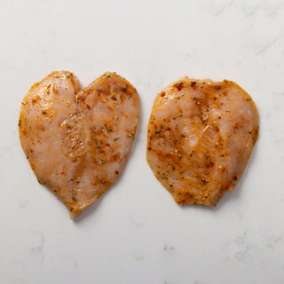 Two seasoned chicken escalopes on a white marble surface