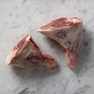 Two raw lamb shanks on a marble surface