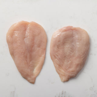 Two raw chicken breast escalopes on a white marble surface