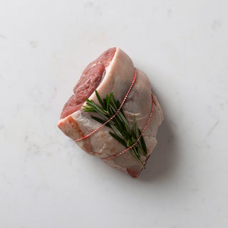 A tied boneless rump of hogett with rosemary on a marble surface.